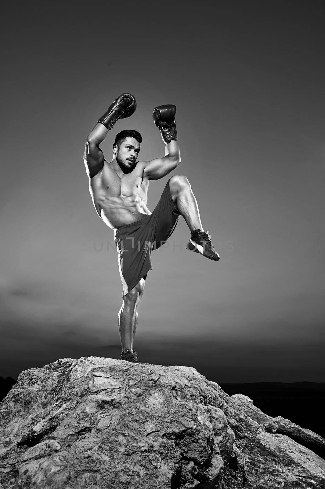 Black and white shot of a male fighter performing kickboxing outdoors training and working out exercising martial combat strengthen powerful energetic active athletics muscles torso abs body concept.