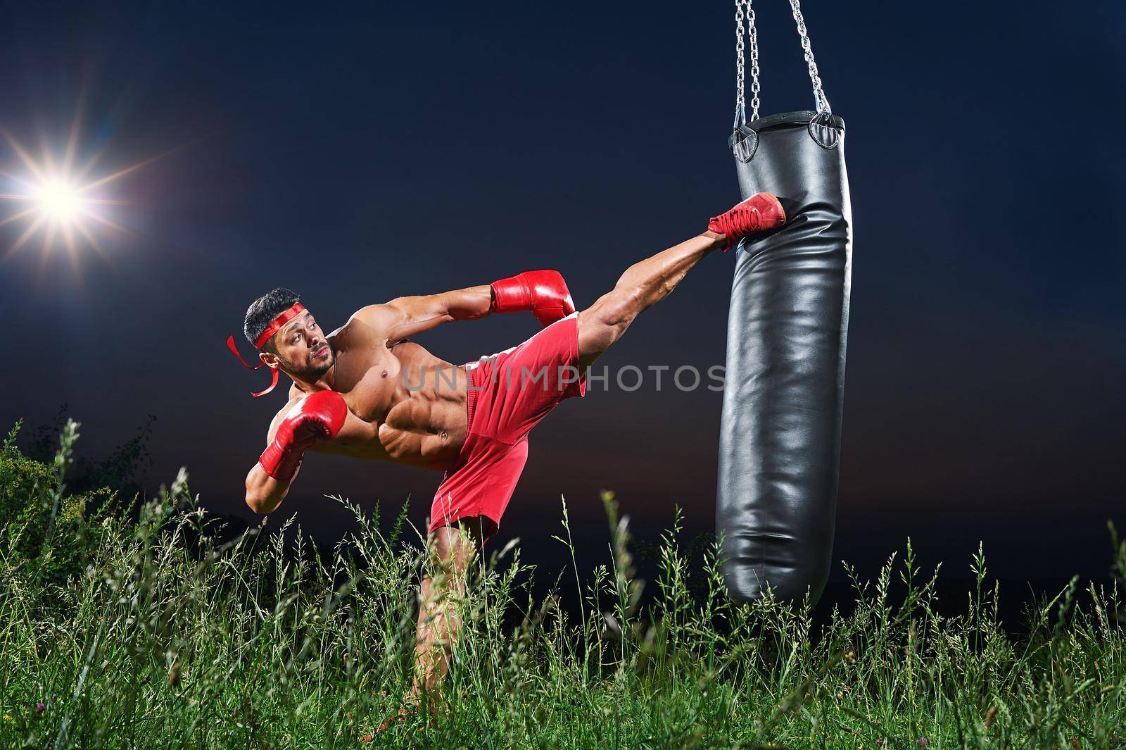 Horizontal shot of a kick boxer working out with a punching bag outdoors at night copyspace kicking training sports sportive motivation fitness muscles toning fit ripped strong lifestyle professional.