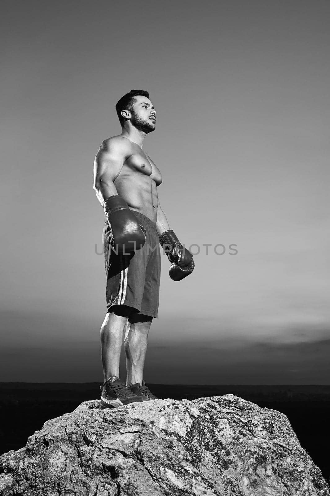 Black and white low angle shot of a handsome young strong muscular athletic man wearing boxing gloves looking away thoughtfully after training outdoors copyspace sports motivation boxer boxing.