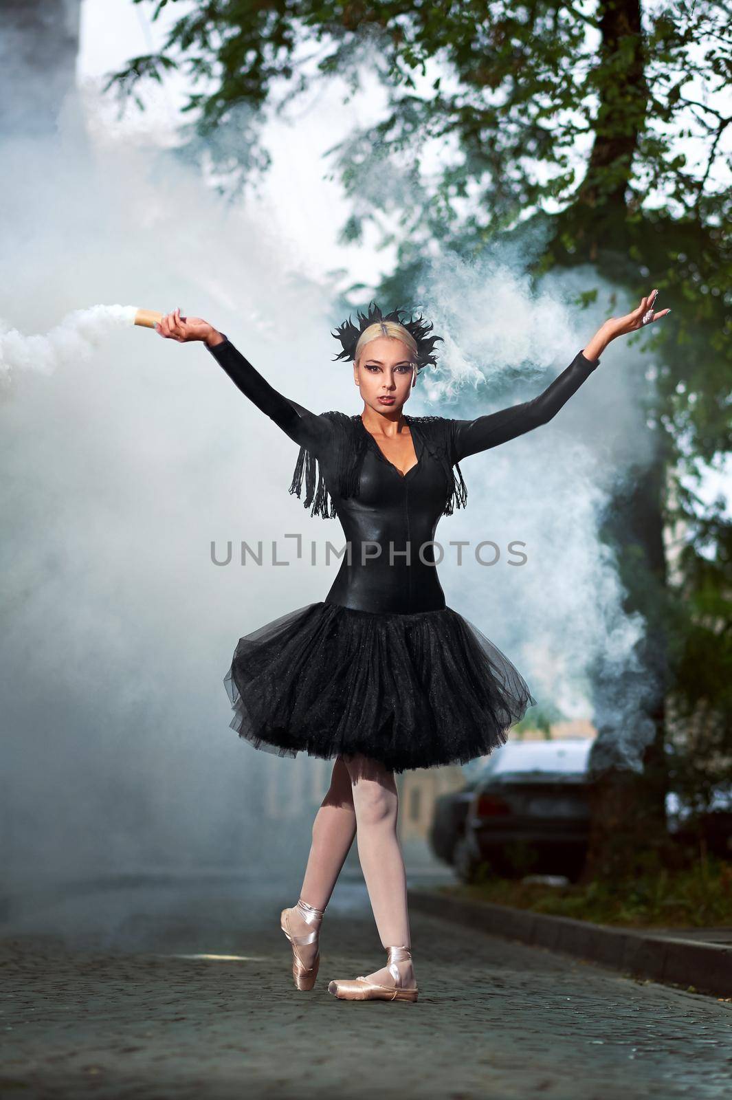 Vertical full length shot of a beautiful blonde haired ballerina wearing black corset and tutu dancing in the city streets smoke on the background dramatic expressive epic performance.