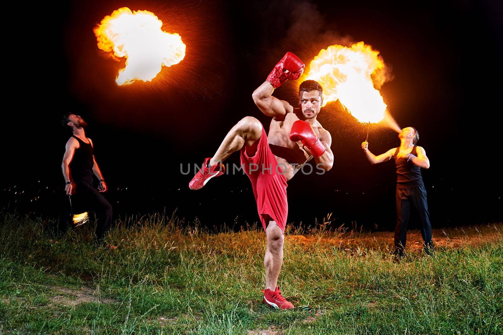 Professional kick boxer practicing outdoors at night fire eaters blowing fire from their mouths on the background creative extreme fiery artists performance champion winning training sports fitness.