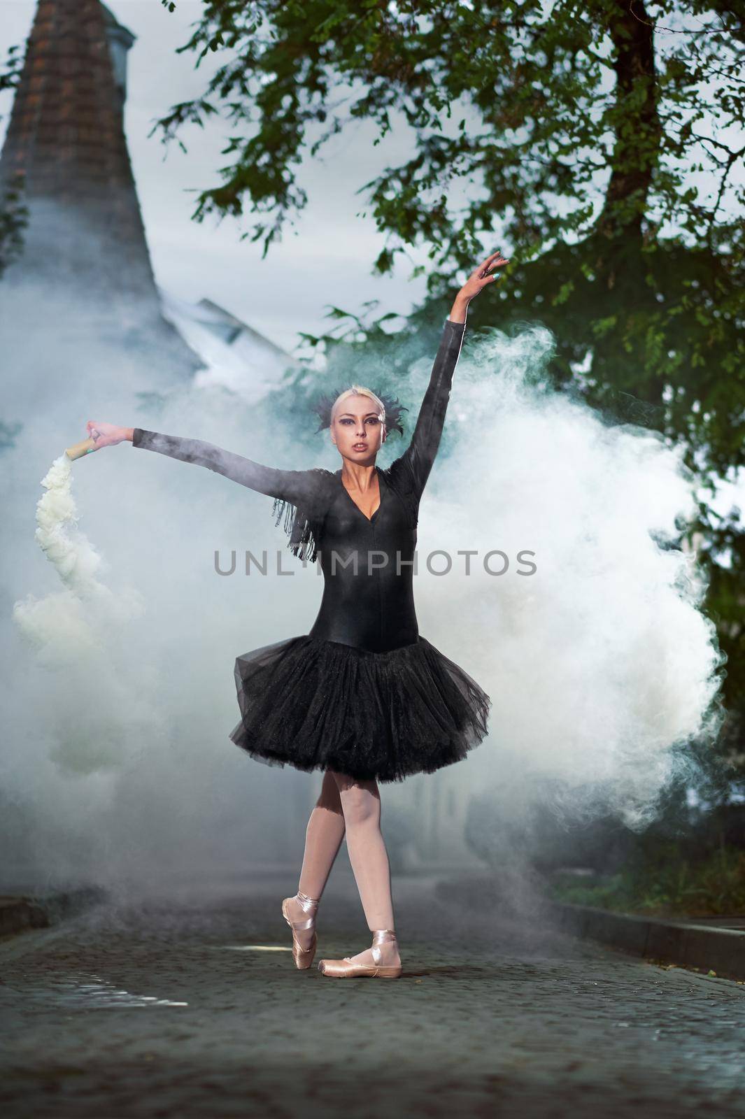Full length shot of a beautiful ballerina in black corset and tutu dancing in the smoking street of an old town expressive artistic confidence fierce vogue.