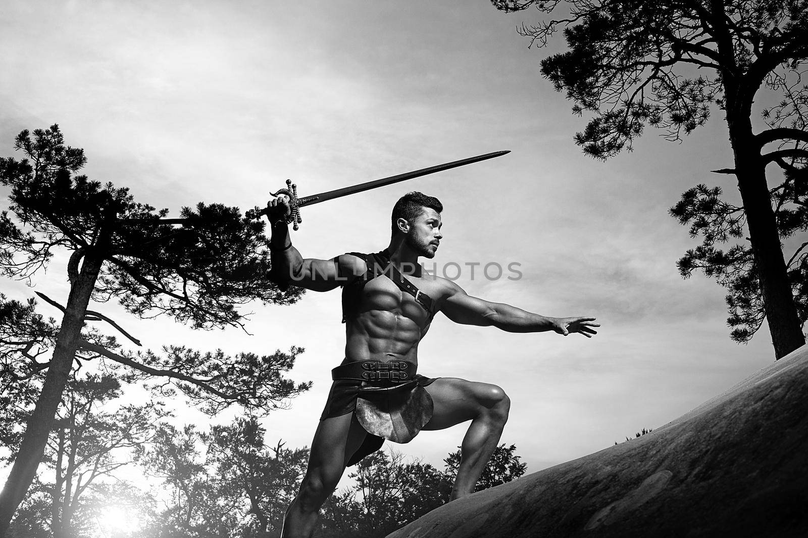 Power in every move. Low angle monochrome shot of a stunning masculine young warrior with a muscular body holding a sword climbing a rock copyspace