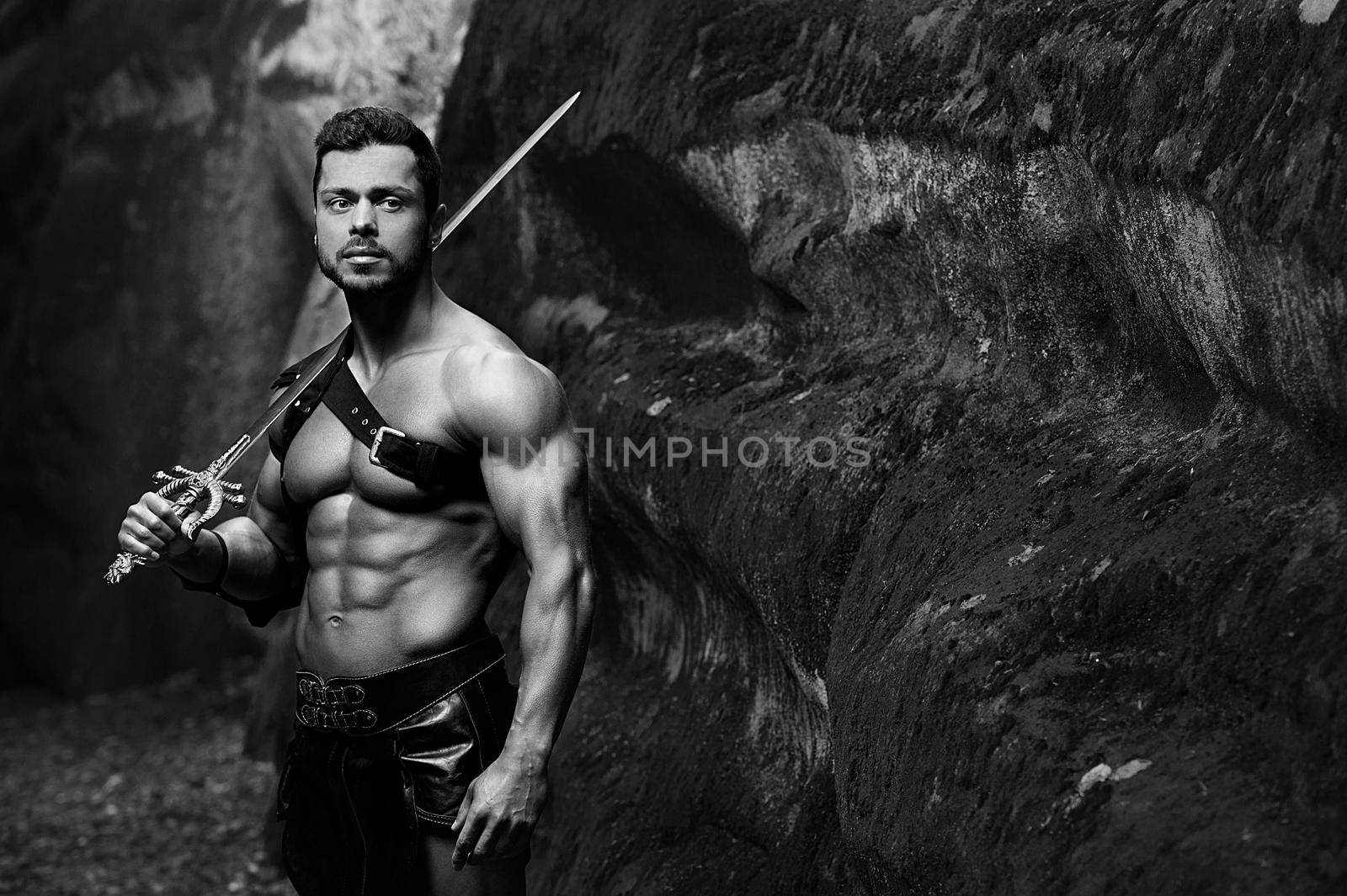 Calmed warrior. Monochrome shot of a handsome muscular strong young gladiator warrior holding a sword copyspace