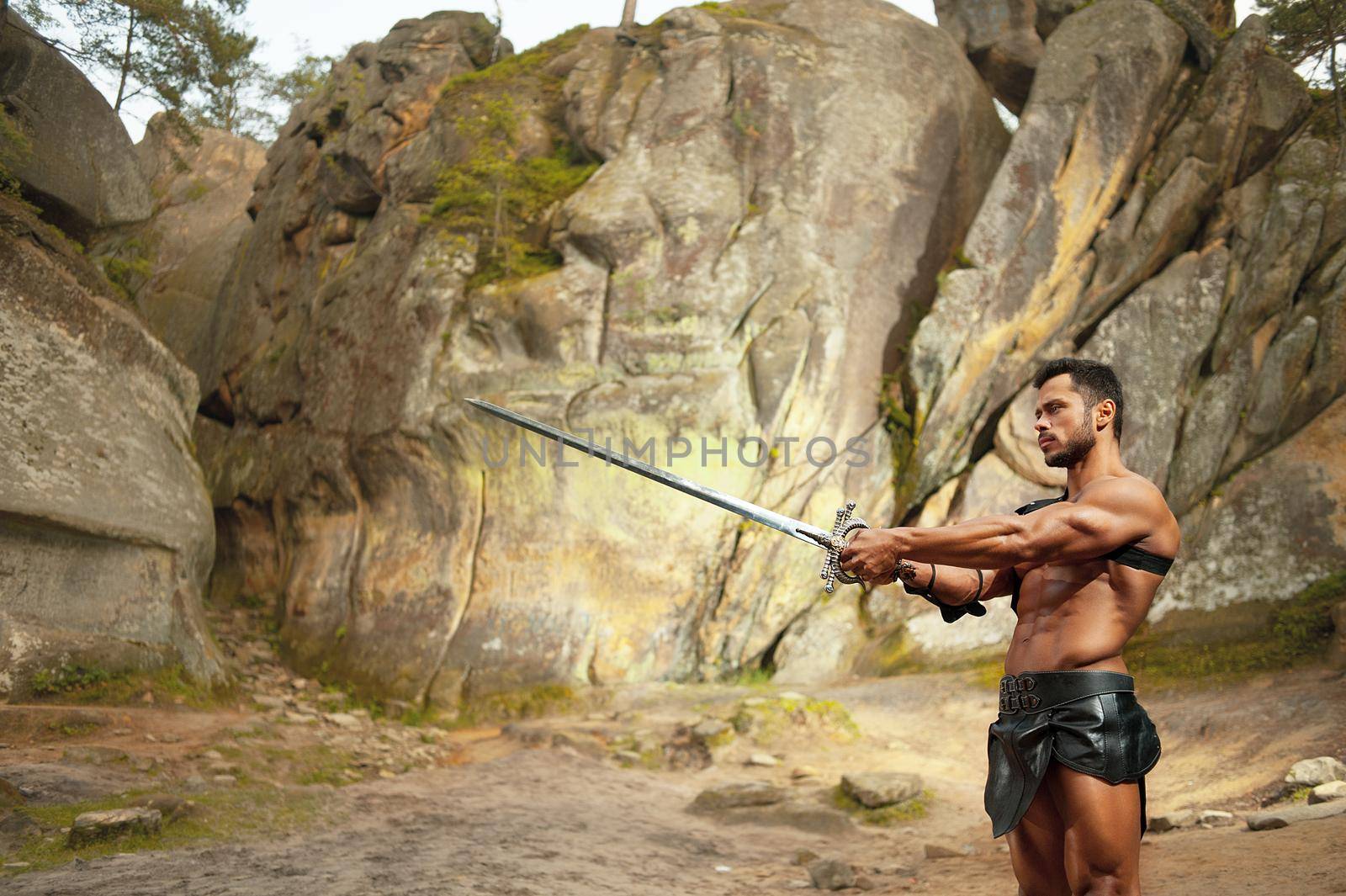 Practicing his skills. Horizontal shot of a masculine Spartan warrior practicing with a sword near the rocks