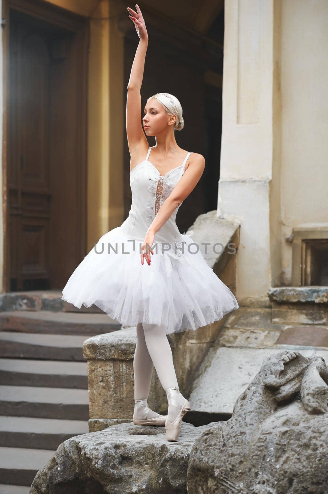 Sunning beautiful ballerina posing gracefully on a big stone near an old building outdoors.
