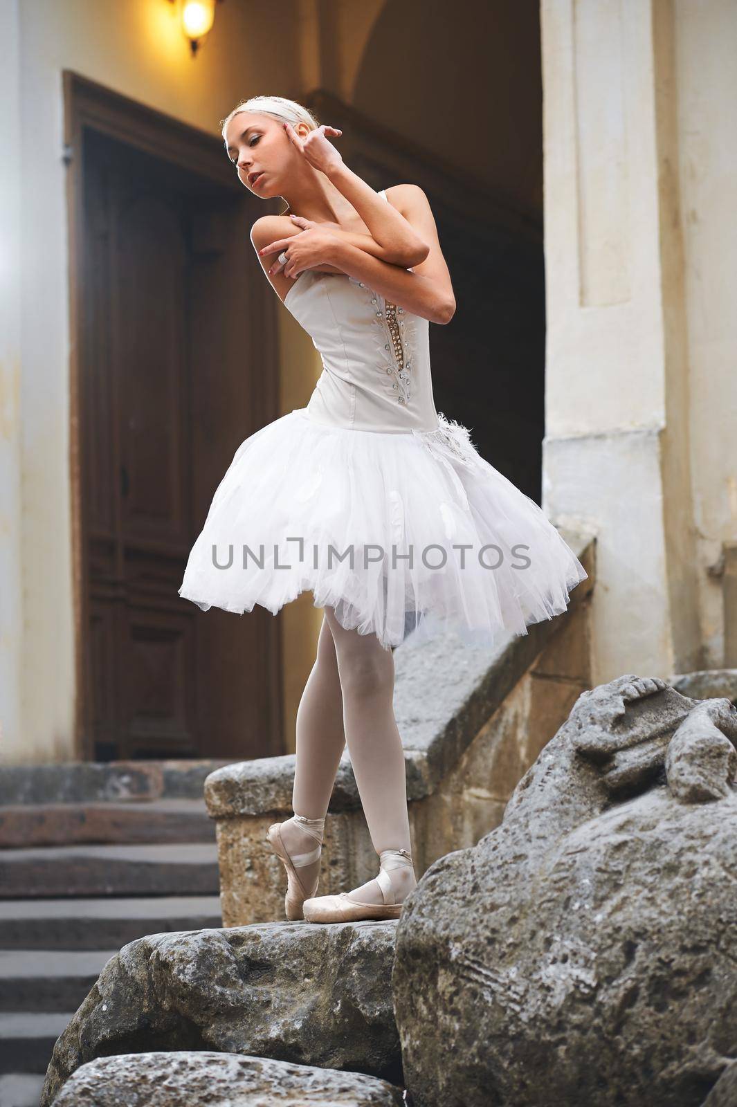 Shot of a stunning beautiful female ballet dancer standing on a big stone near an old fashioned building in the city dancing outdoors posing gracefully.