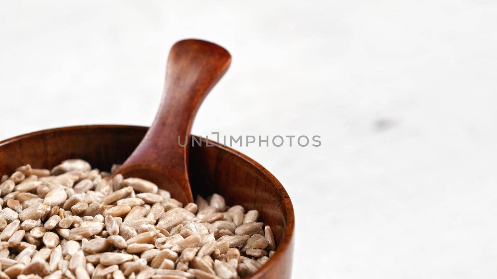 Peeled sunflower seeds in small wooden bowl or cup with spoon on white board, space for text right side.