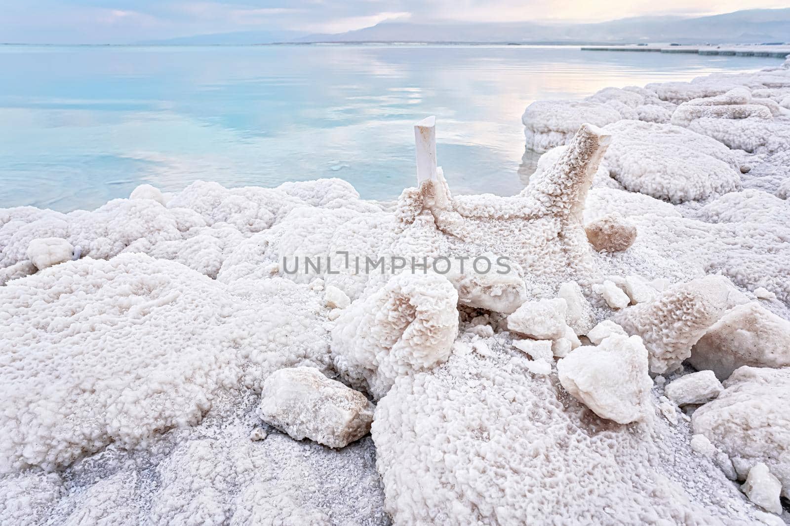 Small plastic chairs completely covered with crystalline salt on shore of dead sea, closeup detail, clear blue water near.