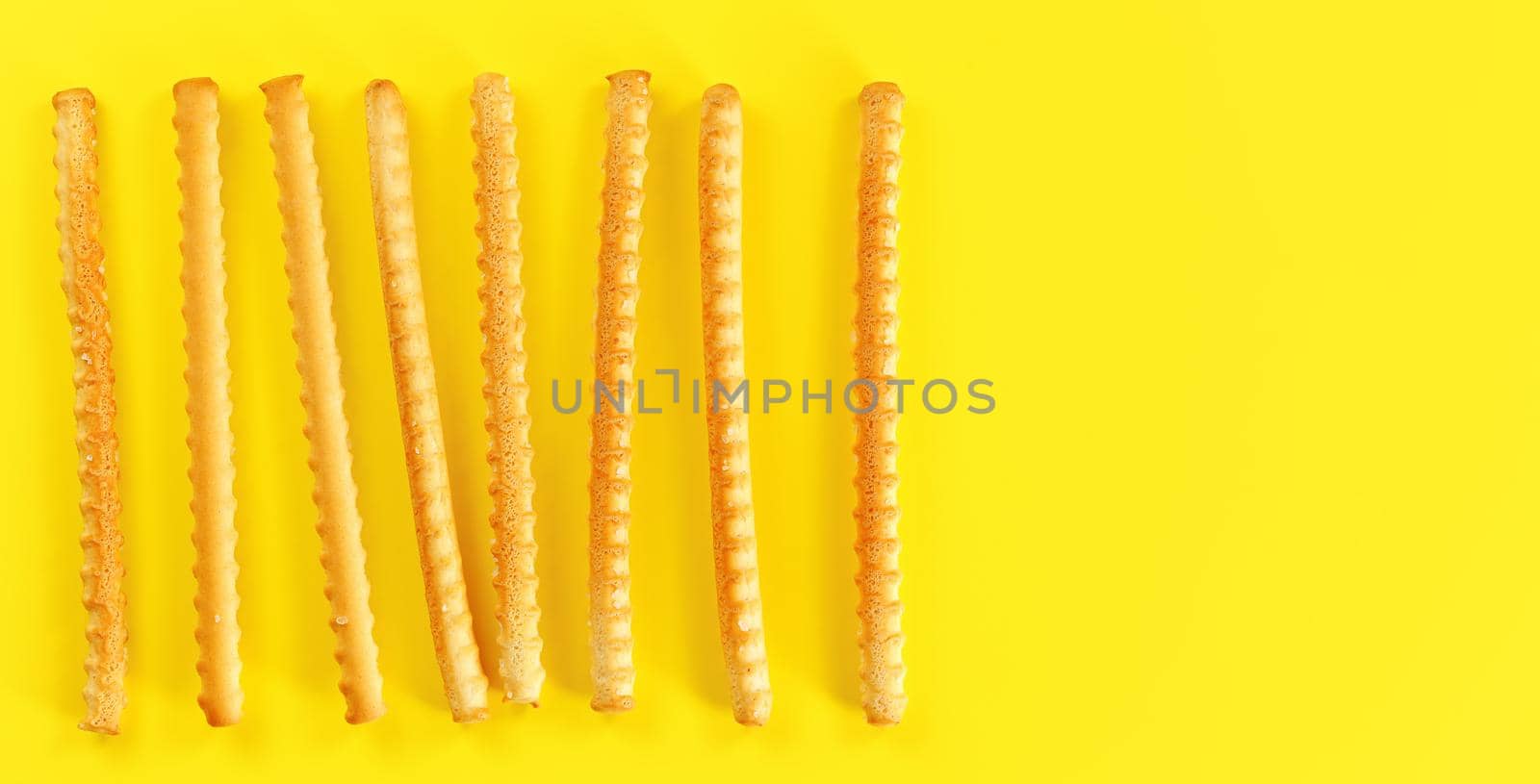 Grissini, also known as breadsticks on yellow board, view from above space for text right side.