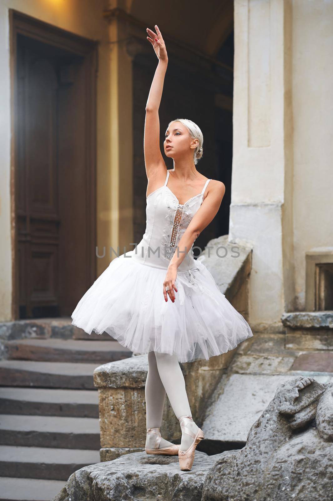 Portrait of a gorgeous young female ballet dancer performing outdoors near an old building standing on a big stone looking away thoughtfully.