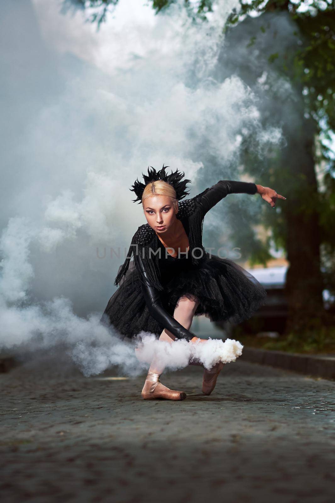 Vertical shot of a black swan ballerina dancing in the smoke on the city streets.