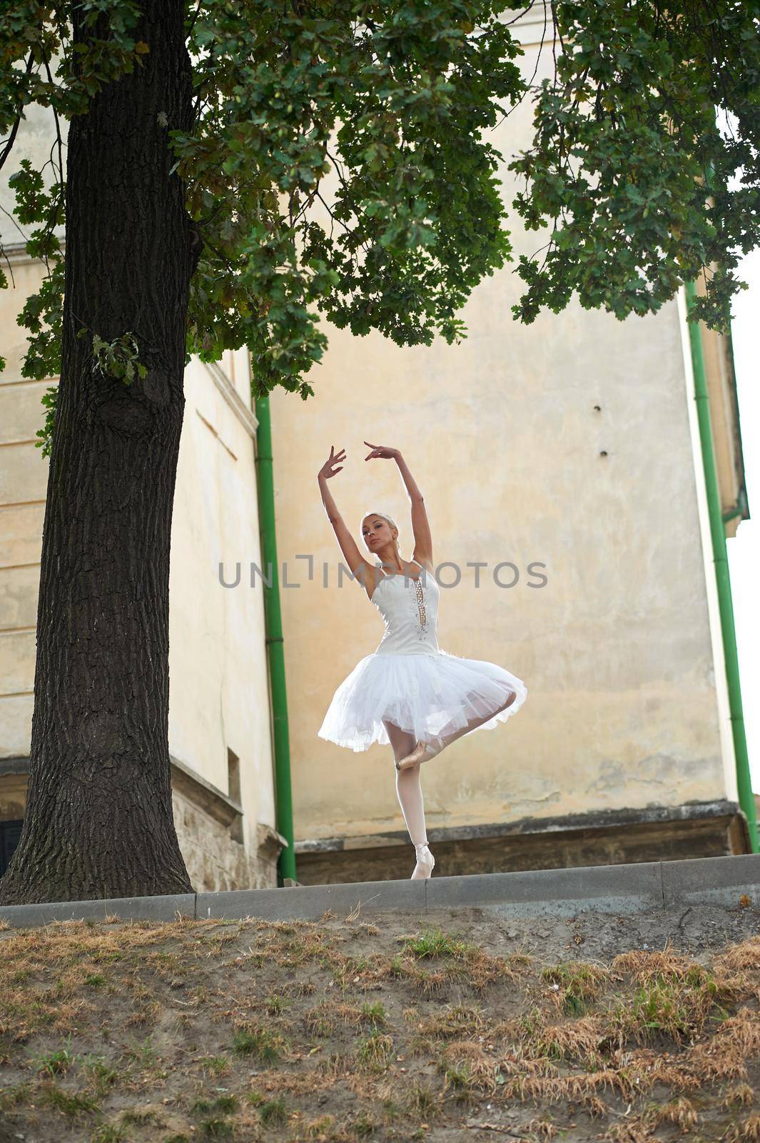 Gorgeous ballerina in white dancing outfit balancing gracefully while performing outdoors.