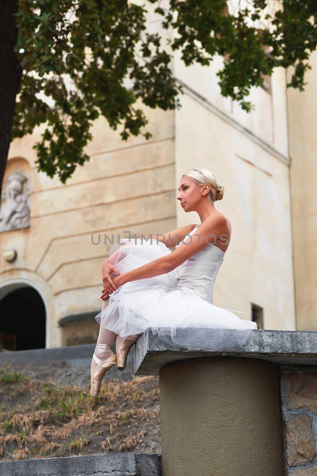 Vertical shot of a beautiful female ballet dancer sitting alone outdoors on the street of the city beauty elegance femininity sensuality artistic concept.
