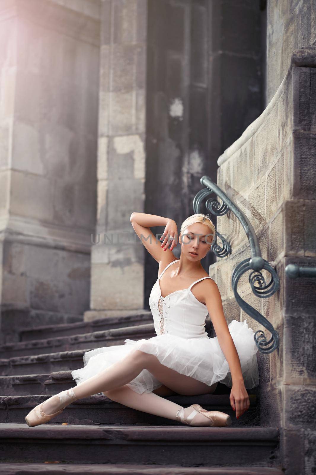 Ballet dreams. Beautiful young ballet dancer woman touching her face gracefully sitting on the stairs