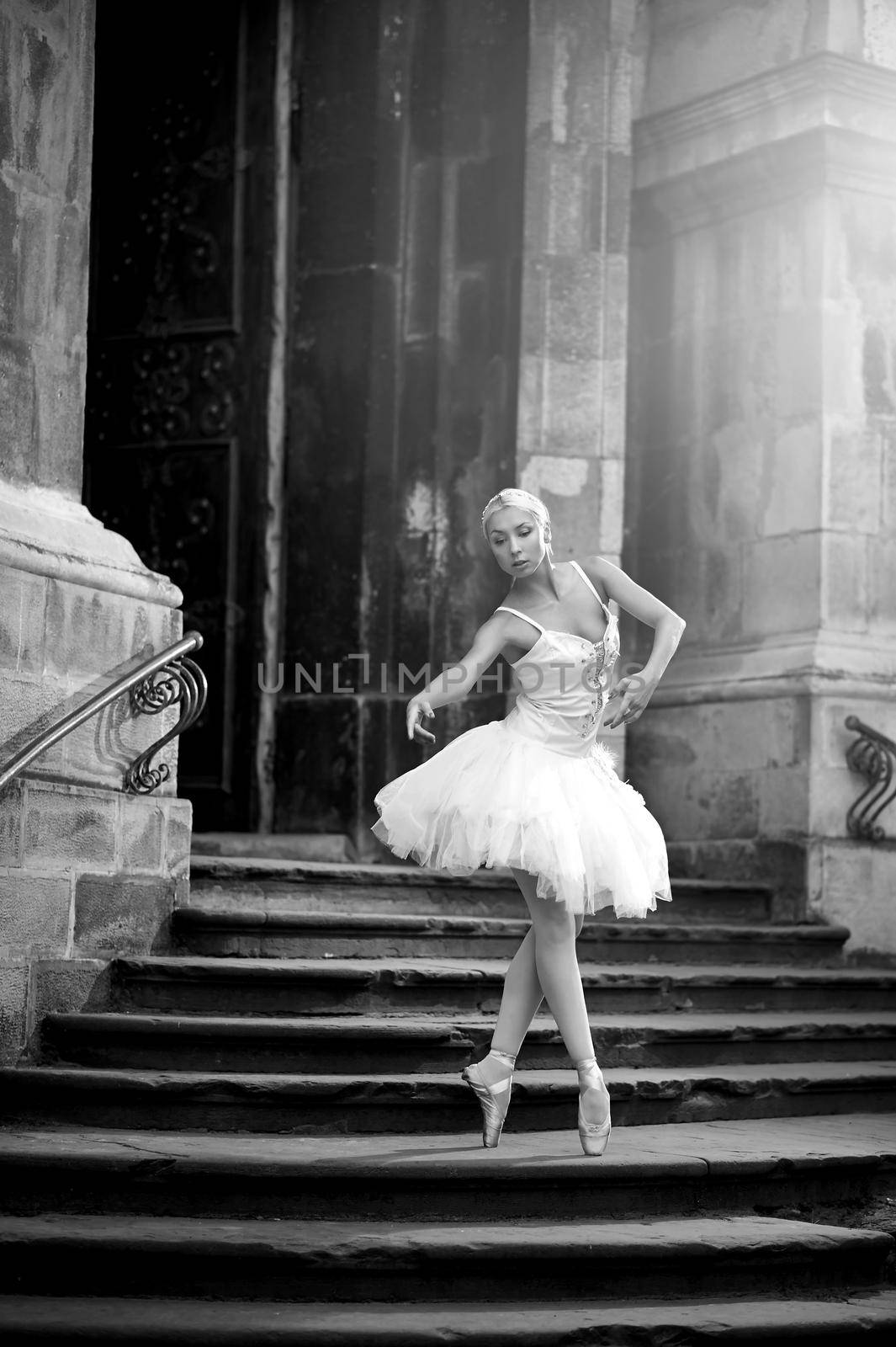 Dancing at any place. Portrait of a beautiful blonde female ballet dancer on an old stairway monochrome shot