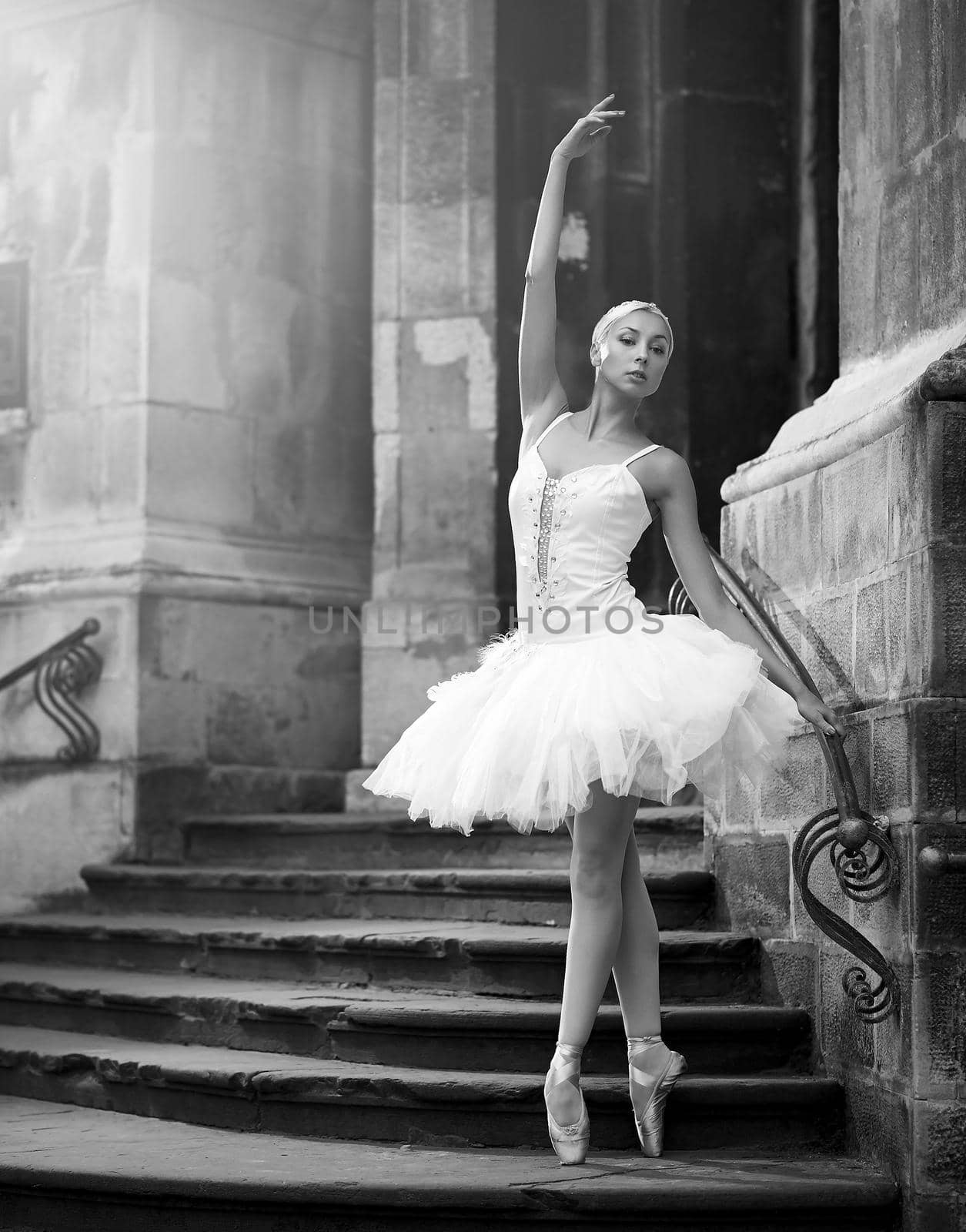 She is a living art. Vertical monochrome shot of a beautiful ballerina standing in ballet pose on stairs of an old castle soft focus