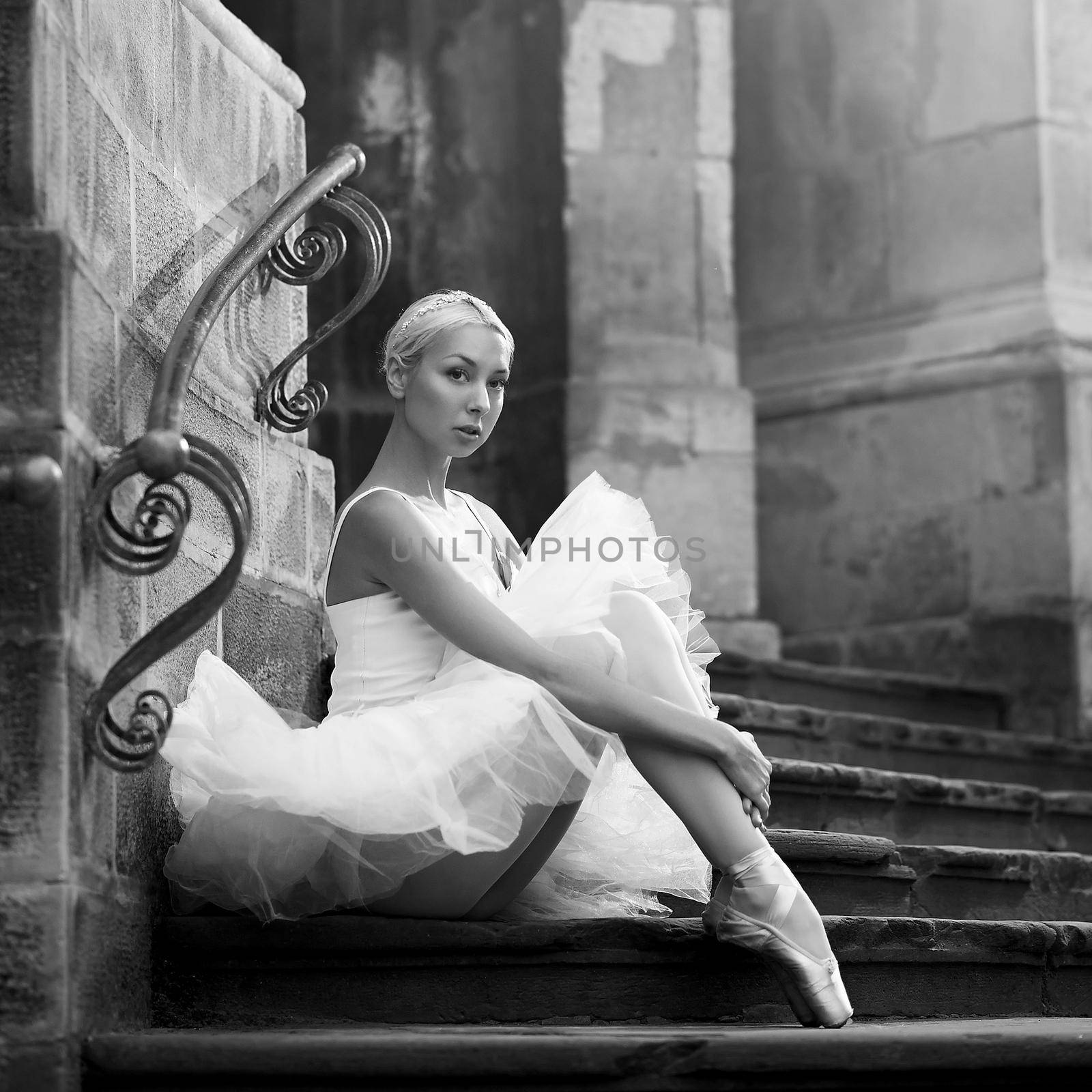 So untouched and innocent. Monochrome portrait of a beautiful ballerina wearing white sitting on the stairs of an old castle