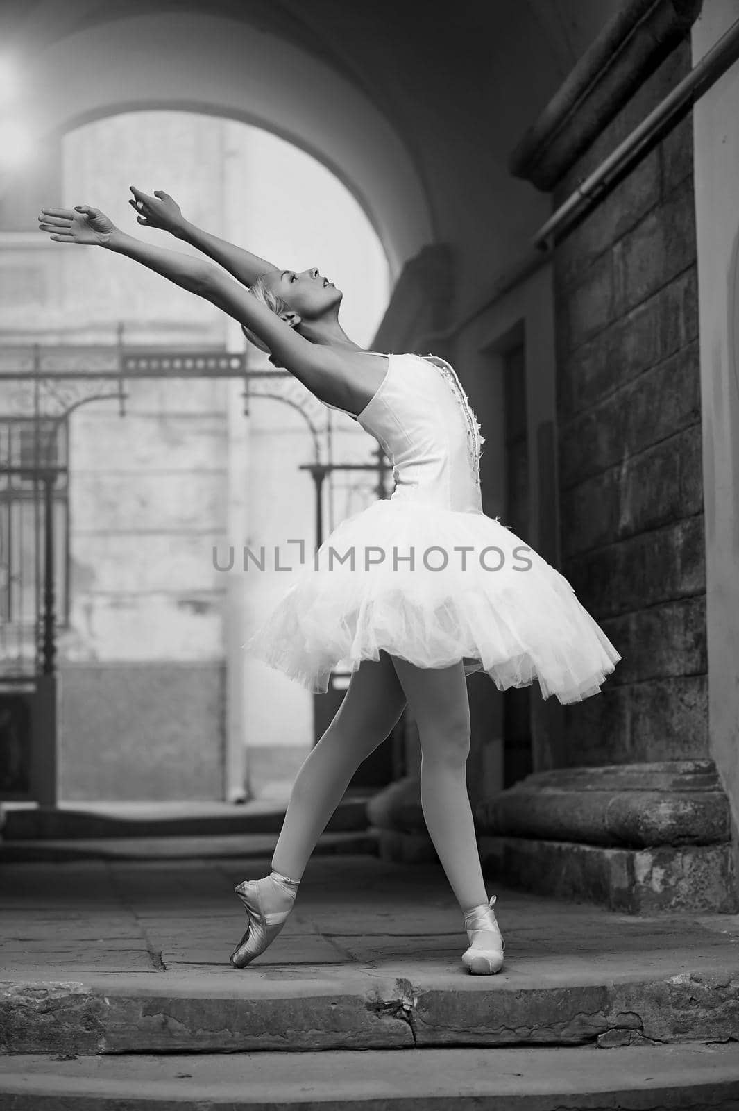 Bringing dance to the city. Monochrome portrait of a woman dancing ballet near an old arch