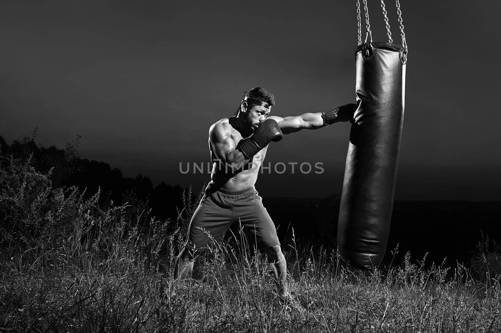 Monochrome shot of an aggressive young boxer hitting punching bag training outdoors copyspace masculinity nature fitness sports athlete athletics activity lifestyle body muscular toughness combat
