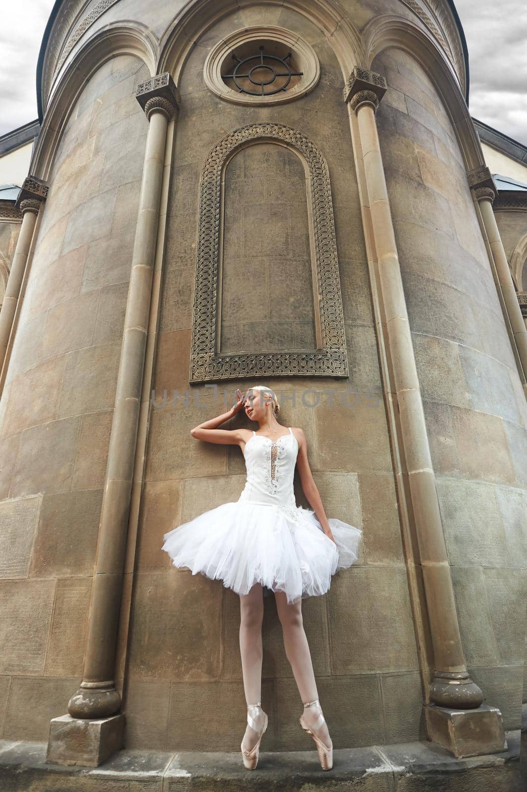 Low angle shot of a stunning elegant ballerina standing near the wall of a beautiful old castle.