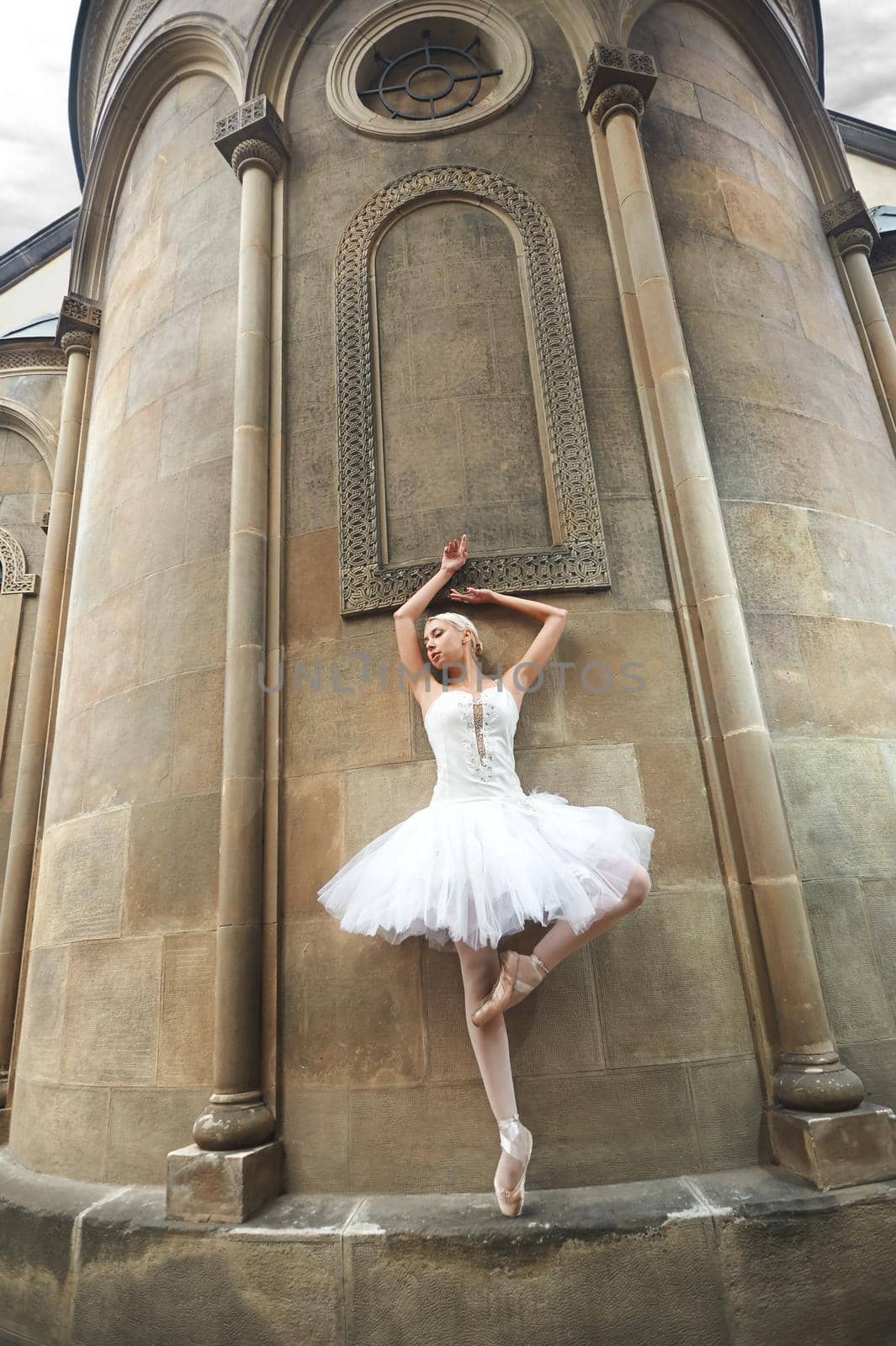 Beautiful young ballet dance posing near an old castle standing gracefully looking away.