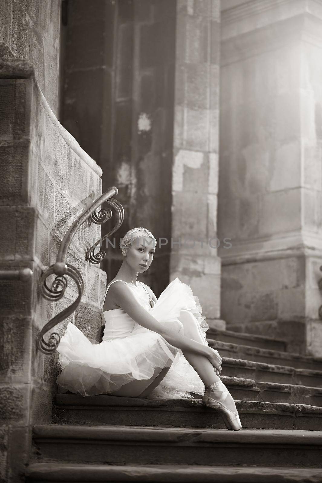 Beam of beauty. Vertical monochrome shot of a gorgeous ballet woman sitting on the stairs of an old house with her arms around her knees soft focus