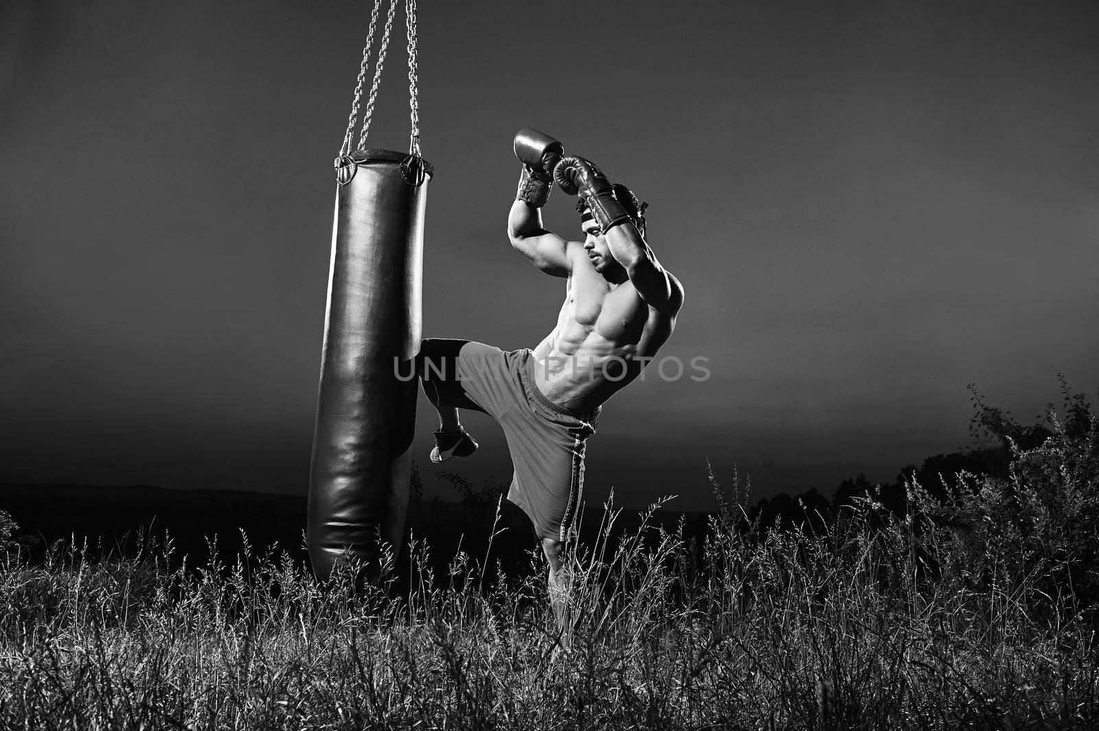 Monochrome shot of a muscular shirtless fighter kicking a punching bag working out outdoors copyspace sports motivation fitness lifestyle fighting fit toned ripped muscular body torso power.