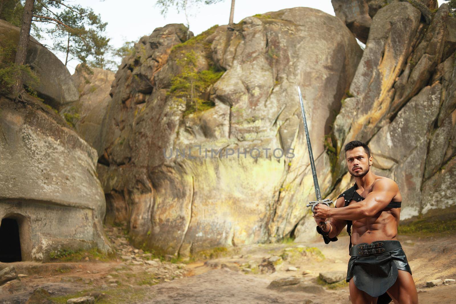 Always ready. Horizontal shot of an ancient warrior posing with a sword near the rocks outdoors copyspace