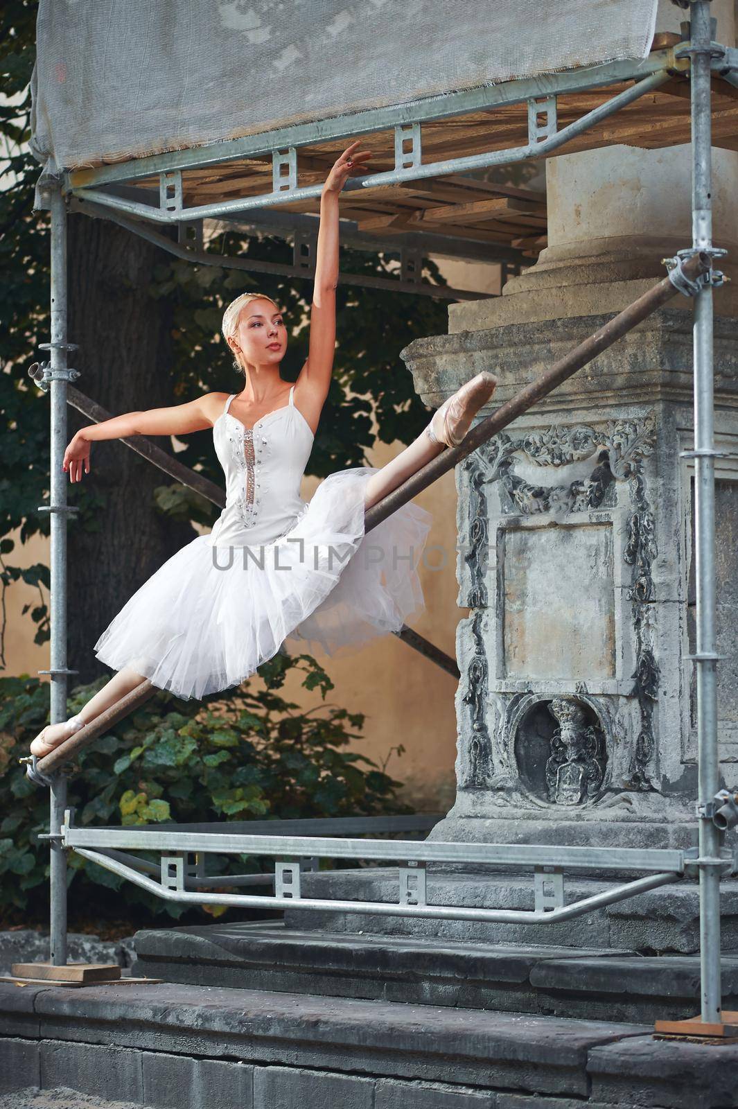 Gorgeous ballerina doing splits balancing gracefully performing on the construction site at the city.