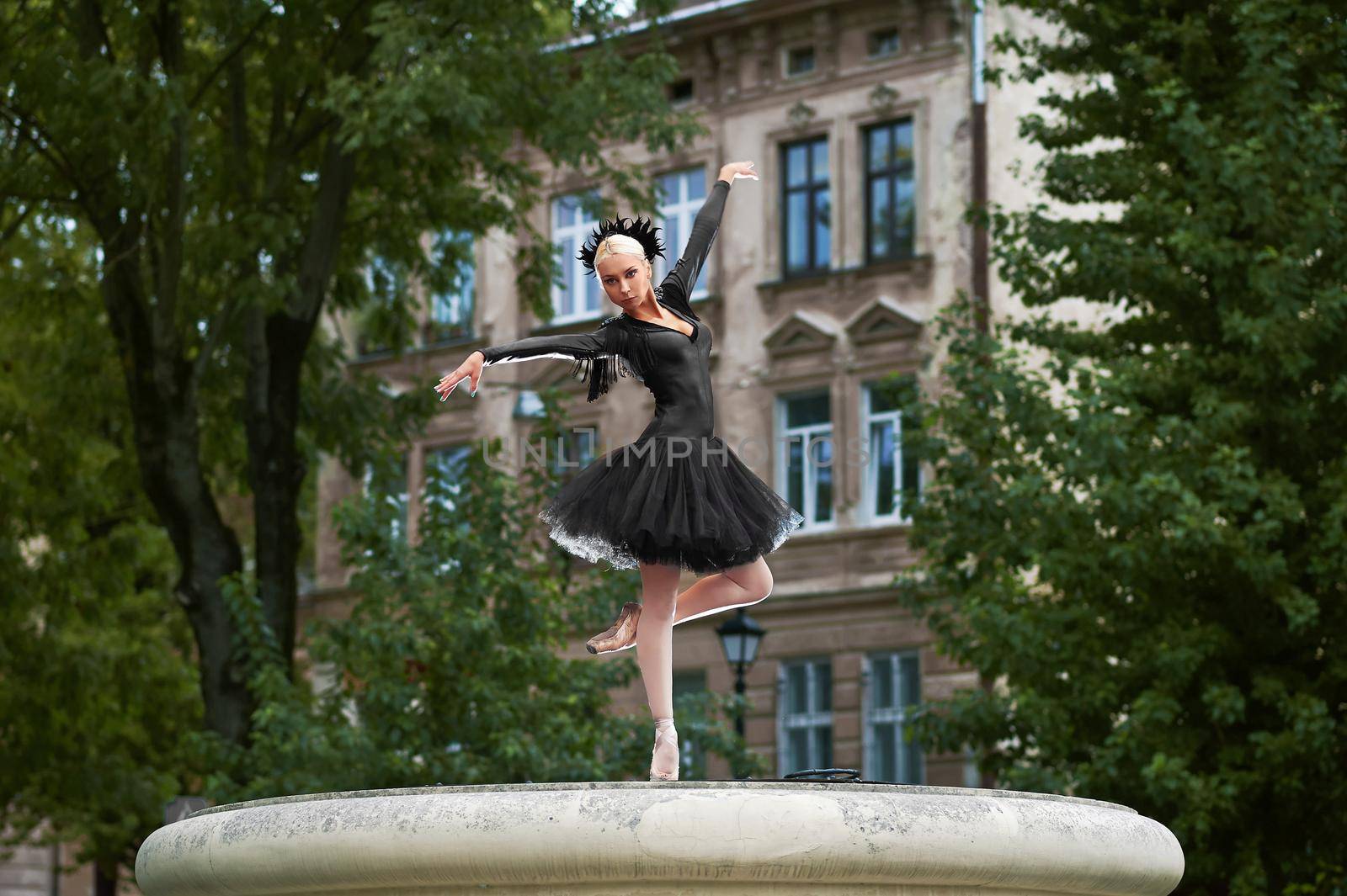 Horizontal shot of a professional ballerina wearing black dress dancing outdoors in the street of an old town.
