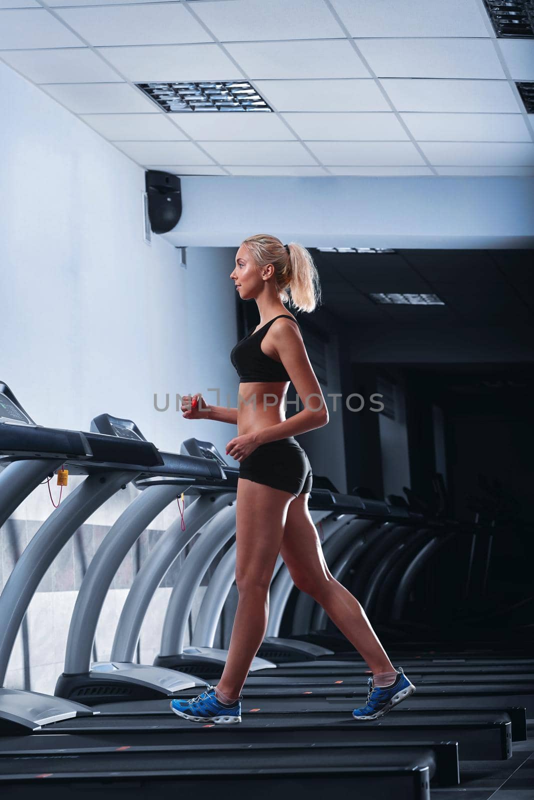 Vertical full length shot of a gorgeous young sportswoman with perfect strong toned body wearing sports top and shorts walking on a treadmill at the gym having her cardio workout at the health club .