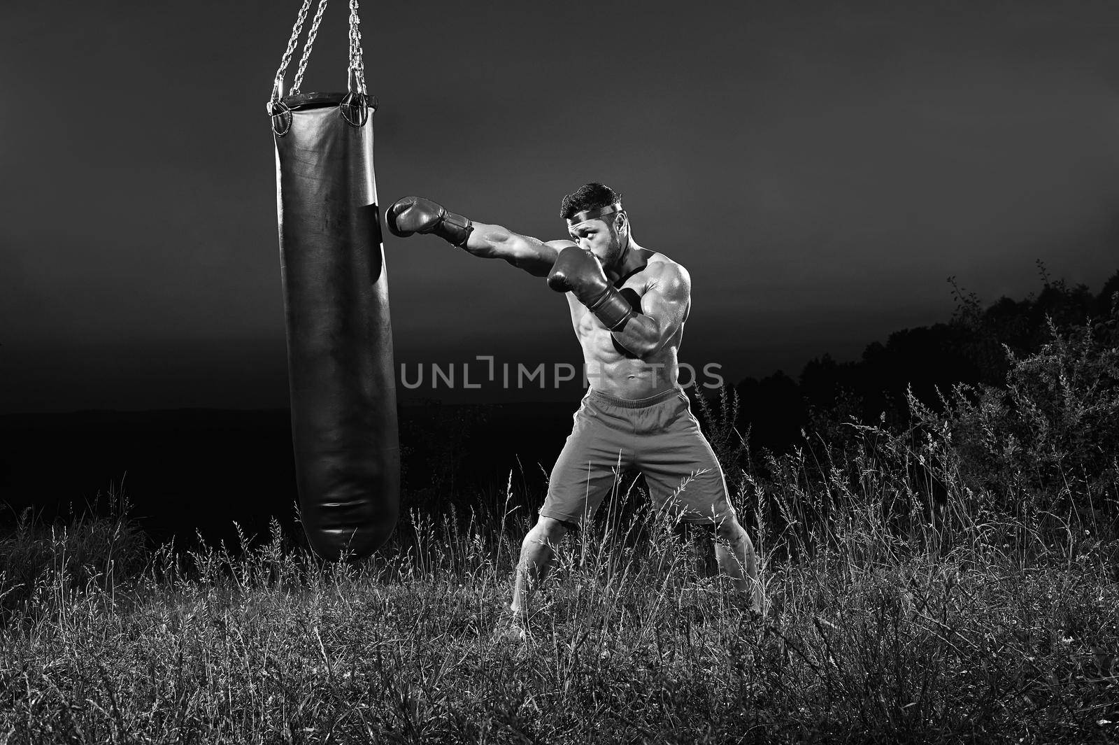 Monochrome shots of a male boxer training with a punching bag ou by SerhiiBobyk