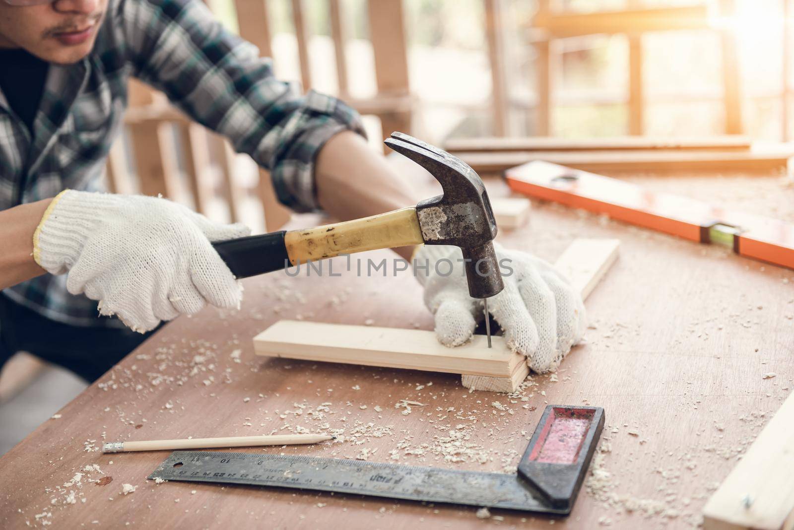 Carpenter Man is Working Timber Woodworking in Carpentry Shop, Craftsman is Hammering a Nail into Timber Frame for Wooden Furniture in Workshop. Workmanship and Job Occupation Concept by MahaHeang245789