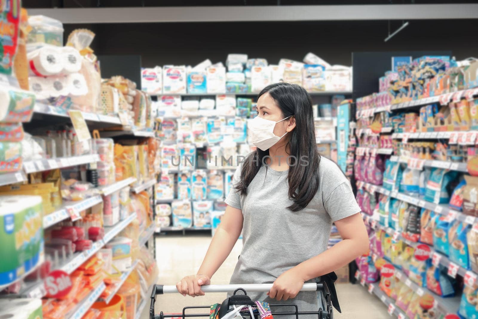 Customer Asian Woman Wearing Face Mask With Shopping Cart in Supermarket Department Store Shop While Choosing and Looking Goods on Shelf During Covid-19 Pandemic. Coronavirus Covid Situation by MahaHeang245789