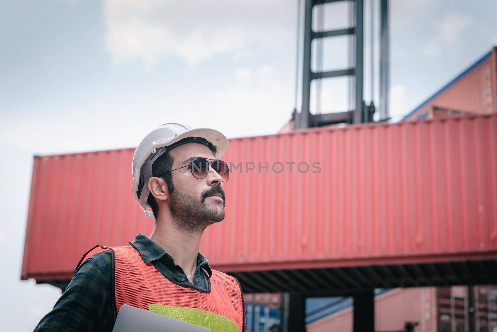 Portrait of Confident Transport Engineer Man in Safety Equipment Standing in Container Ship Yard. Transportation Engineering Management and Container Logistics Industry, Shipping Worker Occupation