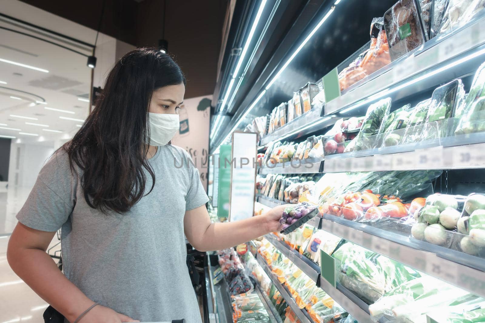 Customer Asian Woman Wearing Face Mask With Shopping Cart in Supermarket Department Store Shop While Choosing and Looking Vegetables on Shelf During Covid-19 Pandemic. Coronavirus Covid Situation 