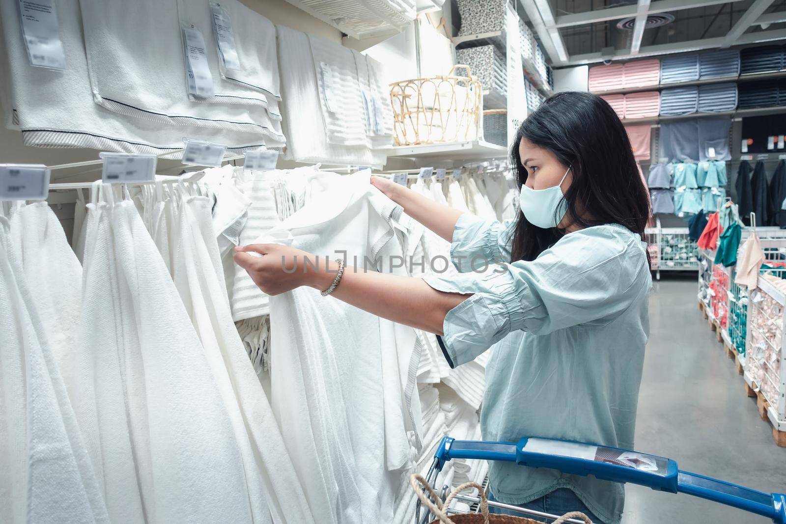 Customer Asian Woman Wearing Face Mask With Shopping Cart in Supermarket Department Store Shop While Choosing and Looking Towels on Shelf During Covid-19 Pandemic. Coronavirus Covid Crisis Situation