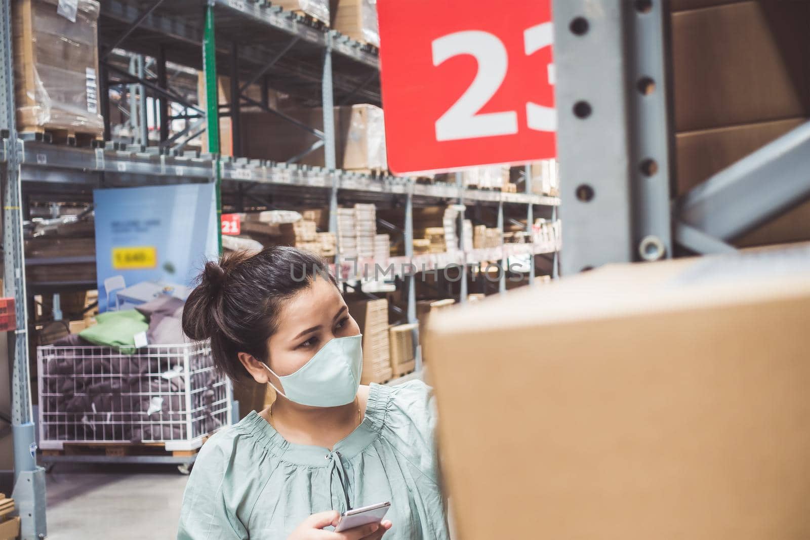 Customer Asian Woman Wearing Face Mask With Shopping Cart in Supermarket Department Store Shop While Choosing and Looking Goods on Shelf During Covid-19 Pandemic. Coronavirus Covid Situation