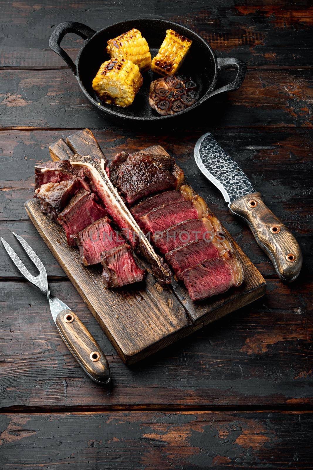 Medium rare dry aged beef steak grilled and sliced set, t bone or porterhouse cut, on wooden serving board, on old dark wooden table background, with copy space for text