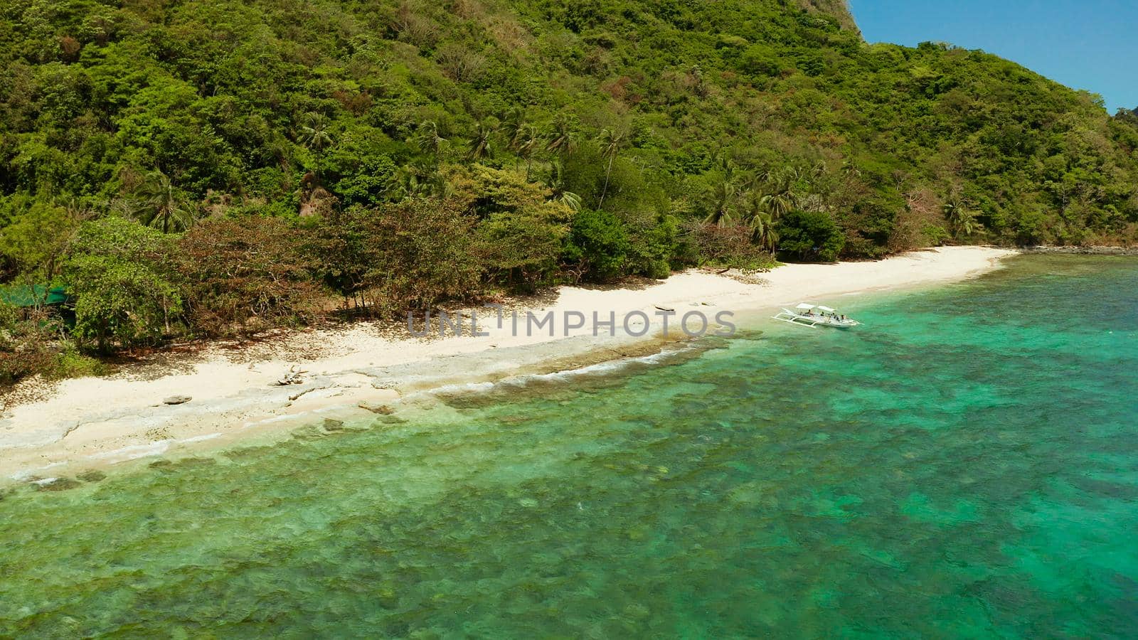 Tropical island with sandy beach, green foliage and palm trees. Lagoon with azure and clear water. Helicopter Island in El Nido, Palawan Philippines. Summer and travel vacation concept