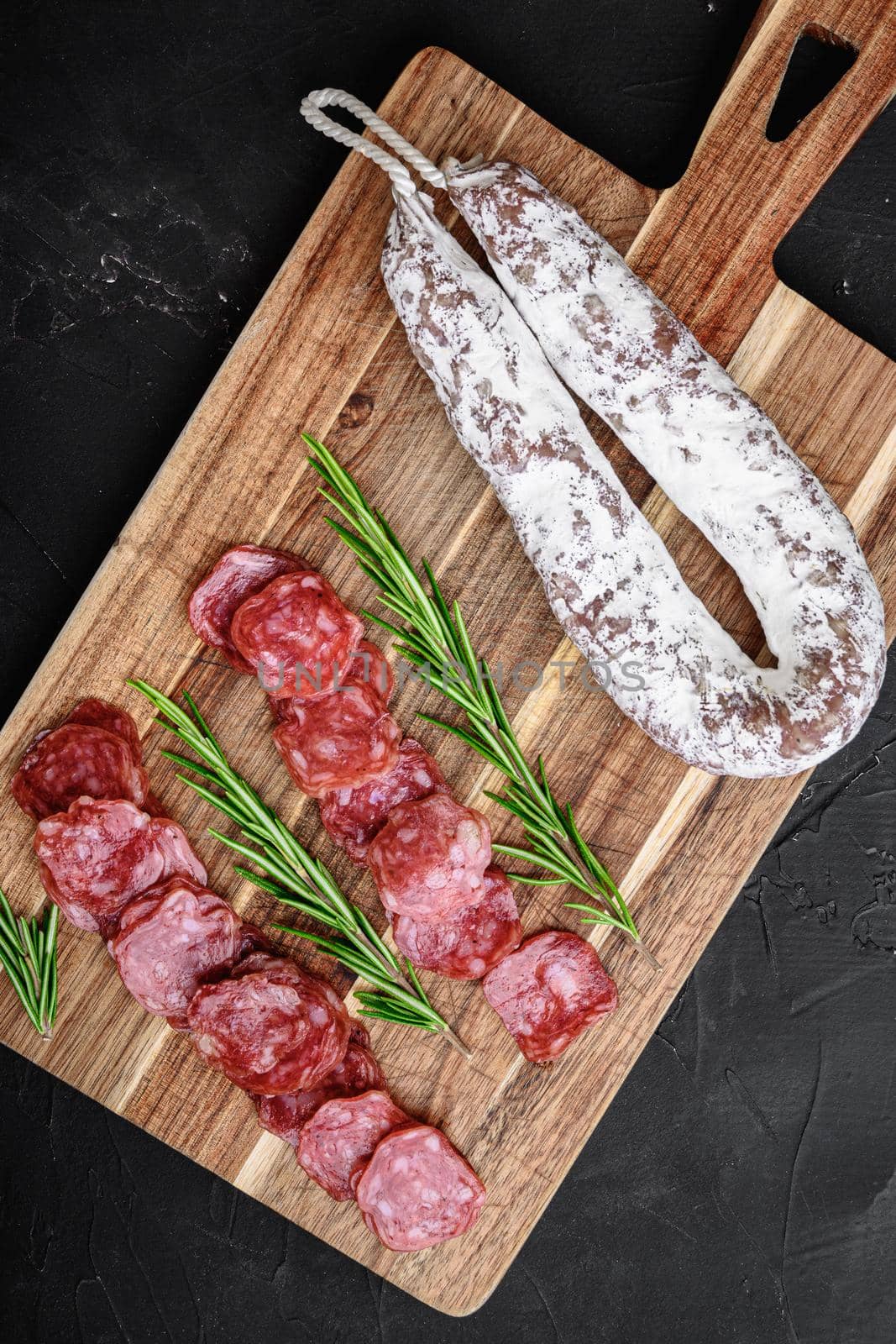 Fuet salami wurst cut in slices and whole sausage on black textured surface, topview.