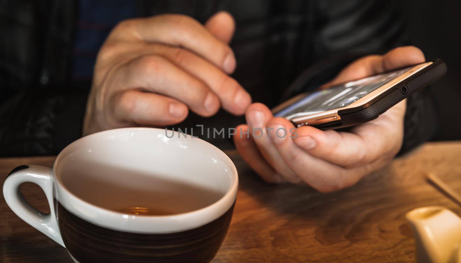 A man is resting in a cafe, drinking tea, reading and writing messages on a smartphone. Work in the mobile office. All-day сommunication. Close-up soft focus image with shallow depth of field
