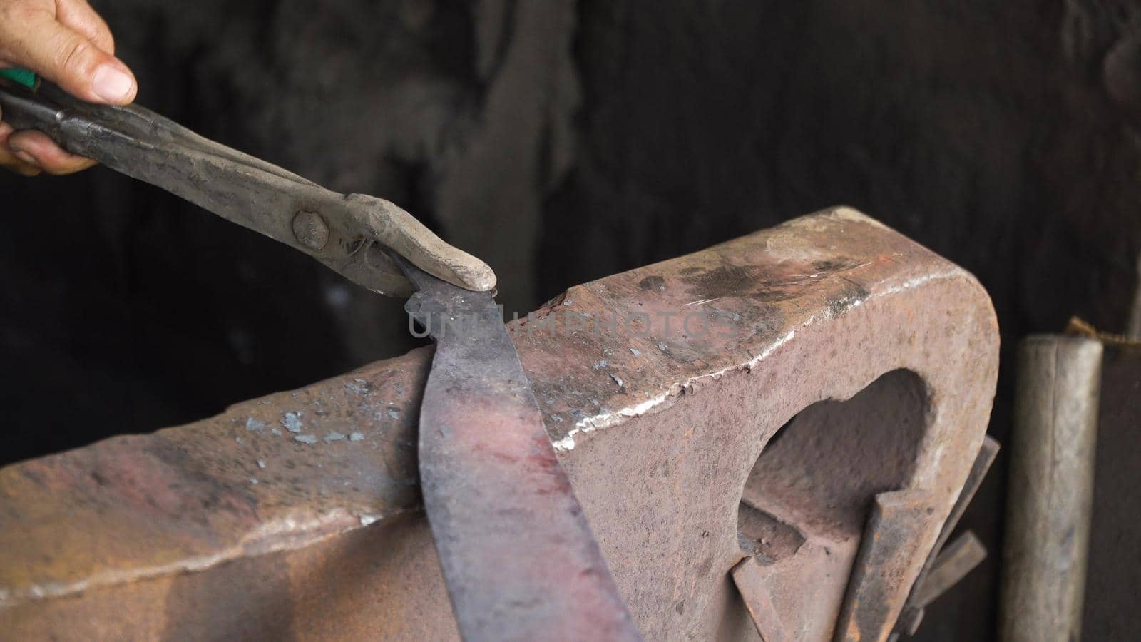 Blacksmith working metal with hammer on the anvil in the forge. hammer forging hot iron at anvil. Blacksmiths make machete. Hands of the smith by the work. Philippines.