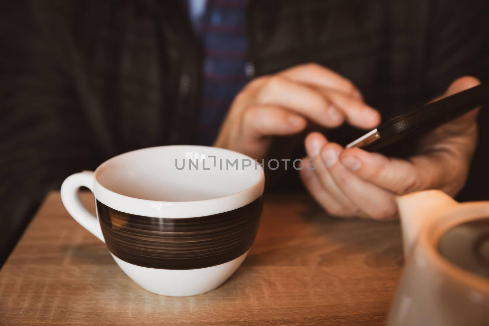 A man is resting in a cafe, drinking tea, reading and writing messages on a smartphone. Work in the mobile office. All-day сommunication. Close-up soft focus image with shallow depth of field