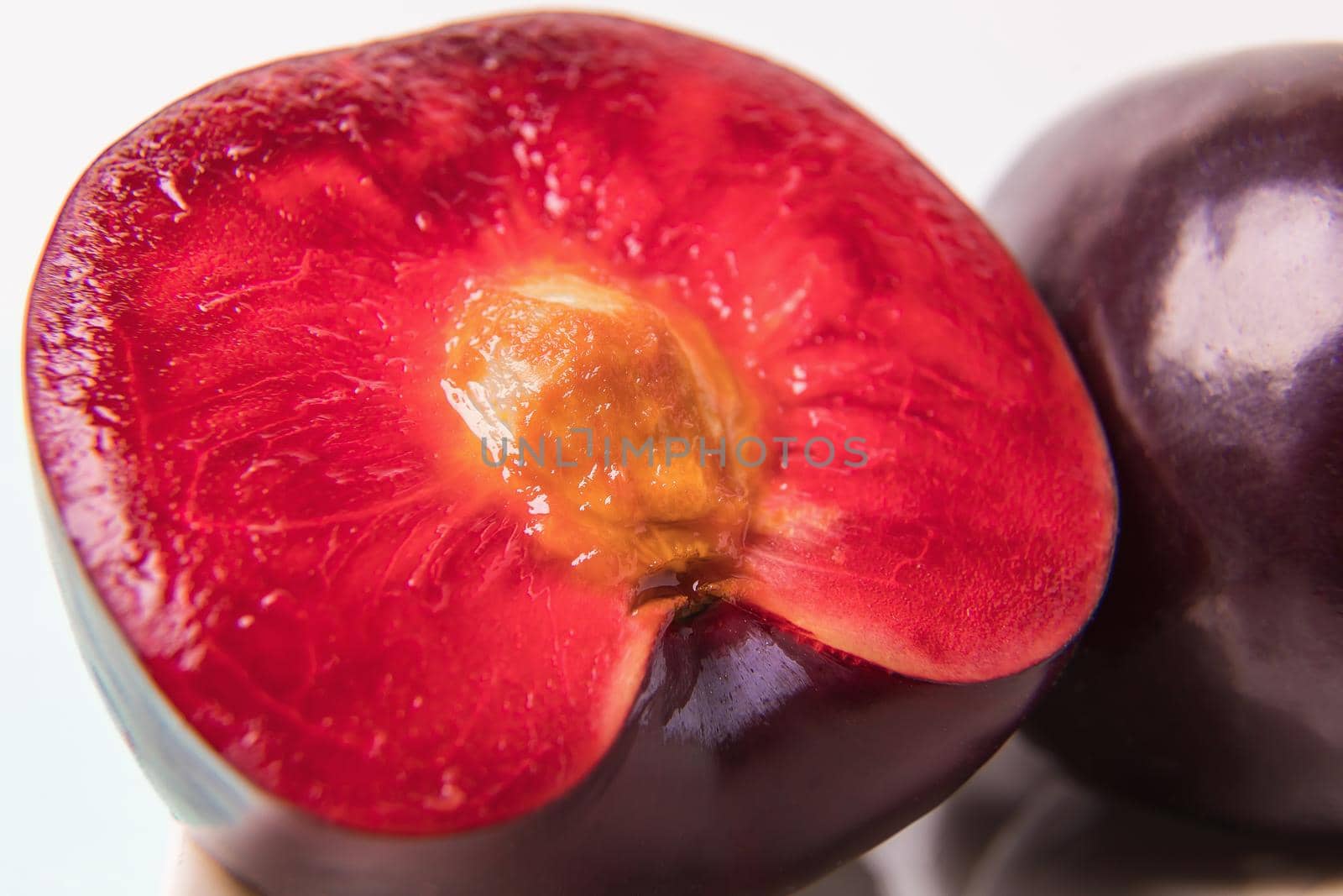 On a white saucer is a large plum, cut in half, and next to it is a whole plum. The pulp of red berries. Close-up.