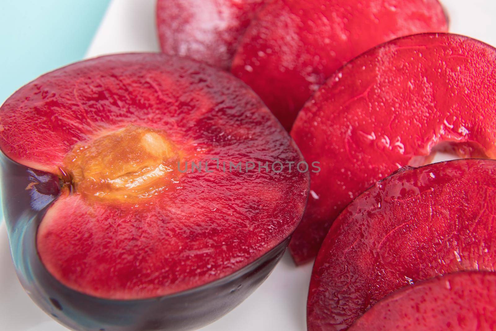 On a white saucer, a large plum, cut in half, with slices next to it. The pulp of red berries. Close-up.