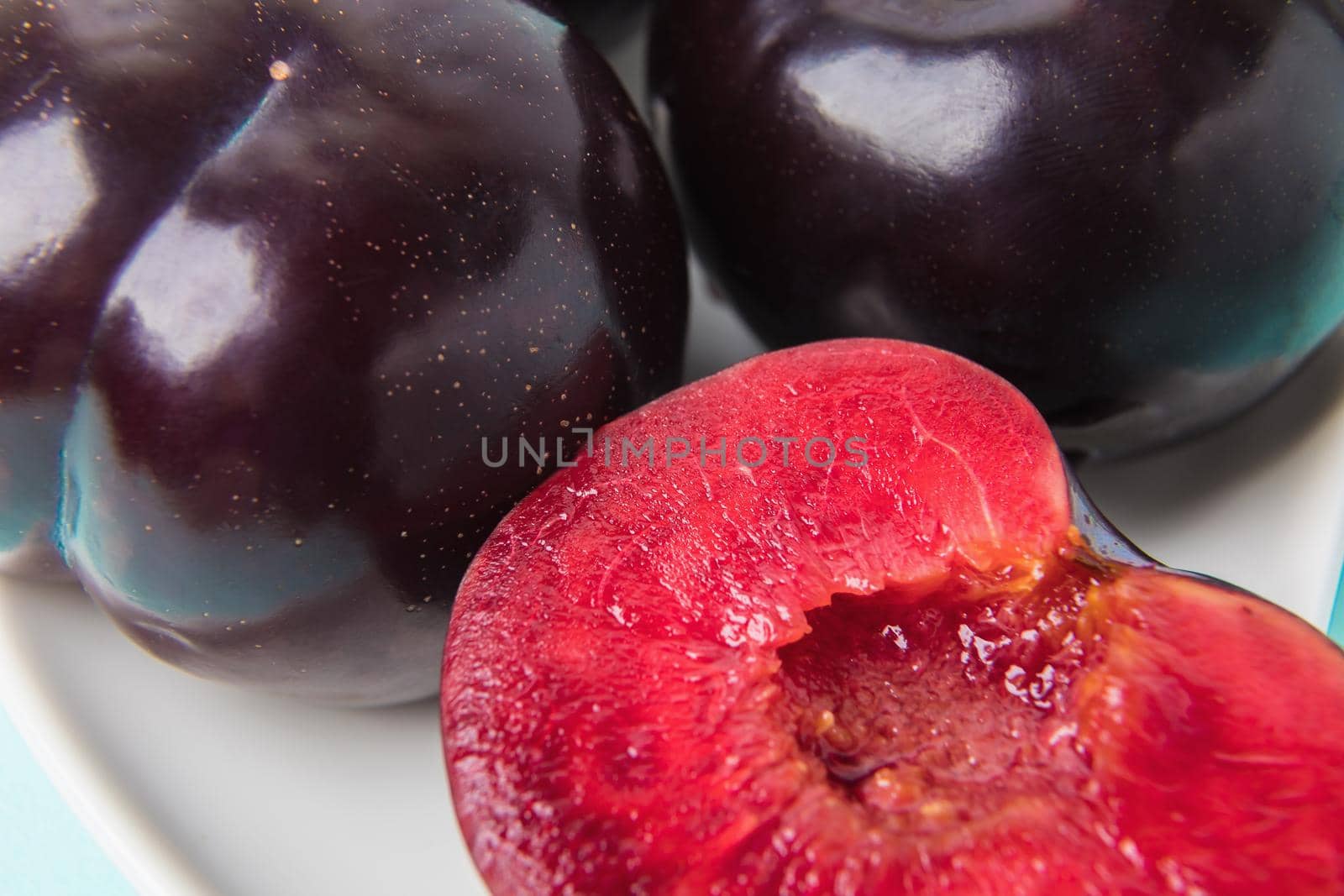 On a white saucer is a large plum, cut in half, and next to it is a whole plum. The pulp of red berries. Close-up.