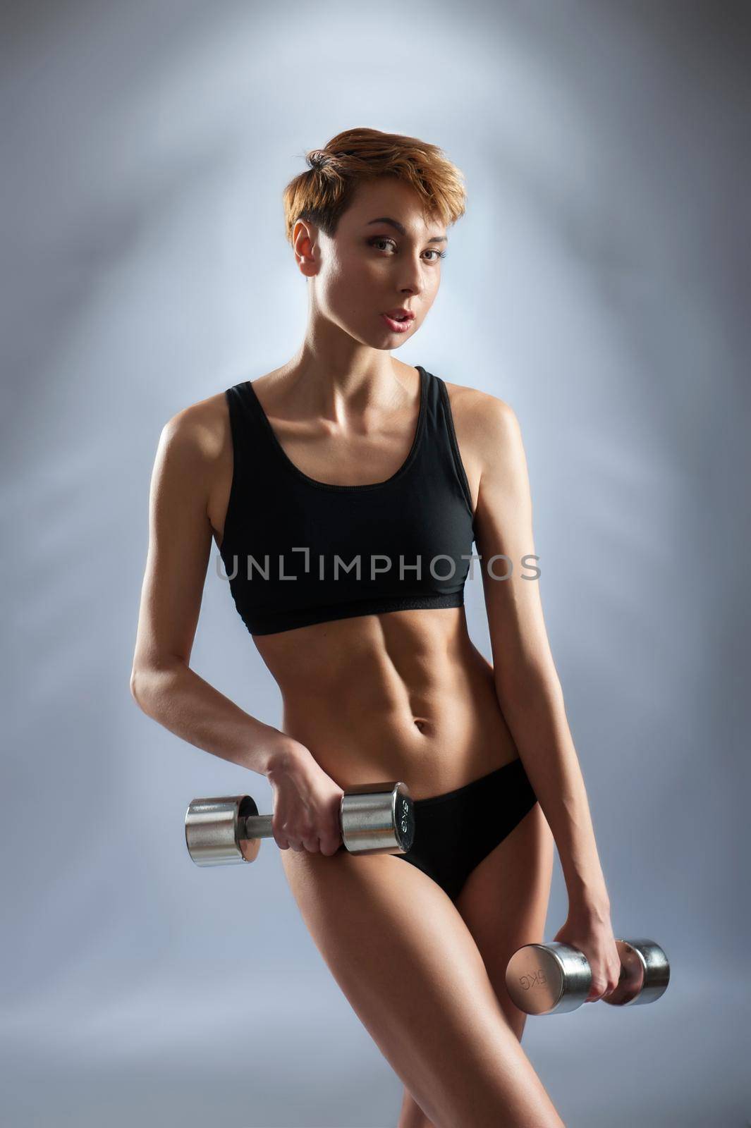 Training routine. Studio portrait of a young short haired fitness woman posing with dumbbells in her hands wearing sport bra and shorts