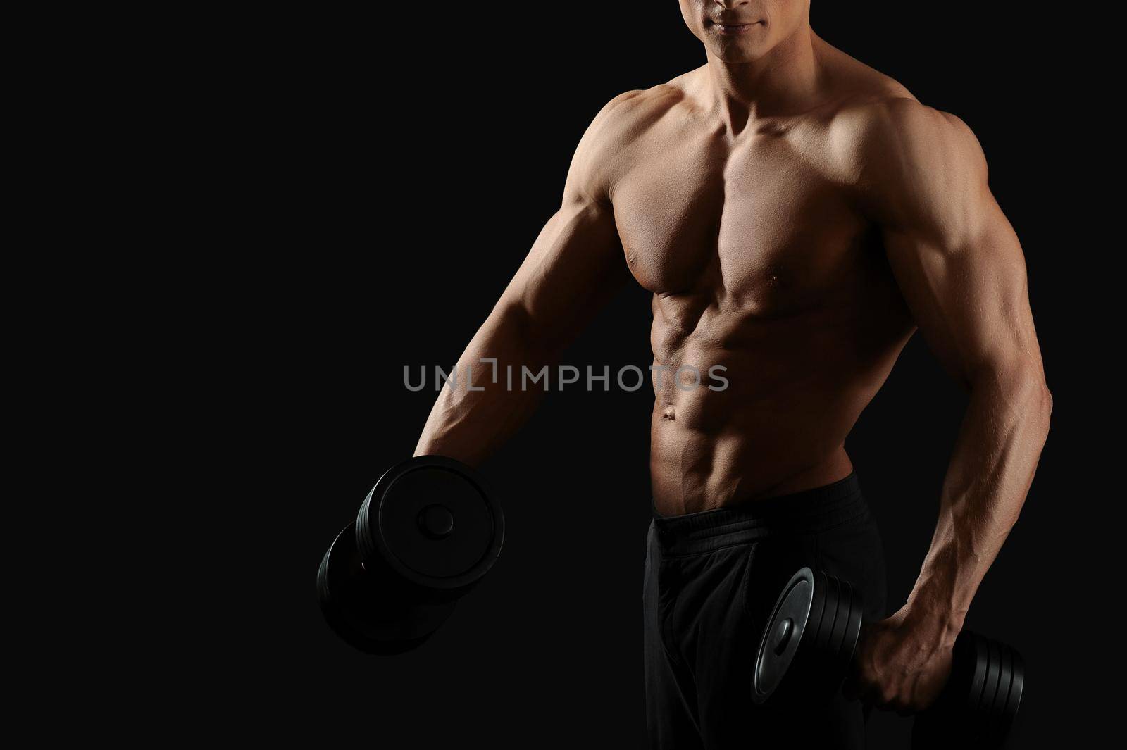 Fitness routine. Cropped horizontal shot of a young fit bodybuilder exercising with dumbbells posing shirtless on black background